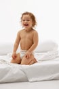 Happy, cute little girl cheerfully smiling with wet curly hair after shower sitting on white bed against white Royalty Free Stock Photo