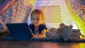 Happy cute little girl having fun playing in teepee tent. Child using digital tablet watching cartoons or playing