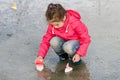 Happy cute little girl in rain boots playing with handmade colorful ships in the spring water puddle Royalty Free Stock Photo