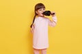 Happy cute little girl singing song on microphone while posing isolated over yellow background, dark haired female chile with Royalty Free Stock Photo