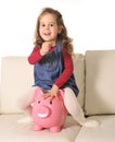 Happy Cute little girl sitting on huge piggy bank inserting Coin