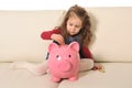 Happy Cute little girl sitting on huge piggy bank inserting Coin