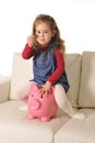 Happy Cute little girl sitting on huge piggy bank inserting Coin