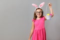 Happy cute little girl wearing easter bunny ears and glasses on gray background. The child is holding a basket of eggs Royalty Free Stock Photo