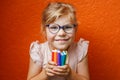 Happy cute little preschooler girl with glasses holding colorful pencils and making gesture while looking at camera Royalty Free Stock Photo