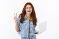 Happy cute redhead female freelancer in denim jacket easily accomplish goal using laptop, show peace victory, goodwill