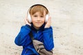 Happy cute schoolboy listening to music in headphones outside school. Kid using wireless headphone