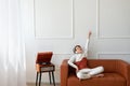 Happy cute teenager boy sitting on brown sofa with hand rising and eyes closed, listening vinyl record on retro wooden turntable Royalty Free Stock Photo