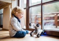 A cute toddler boy sitting indoors at home, playing with robotic dog. Royalty Free Stock Photo