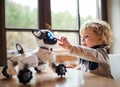 A cute toddler boy standing indoors at home, playing with robotic dog. Royalty Free Stock Photo