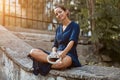 Happy cute woman sitting on ground holding headset. Peaceful atmosphere in park. Listen music and street style concept Royalty Free Stock Photo