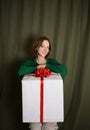 Happy cute woman 35-40 years old with a big white gift box tied with a red bow on dark green background Royalty Free Stock Photo