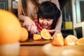 Happy Cute 3-4 Years Old Girl with her Mom Slice some Orange on Wooden Table in Pantry Room. Young Girl is Learning Cook with her