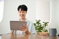 Happy cute young Asian man using his digital tablet at his desk Royalty Free Stock Photo