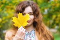 Happy cute young attractive girl with a smile in a fashionable coat stands in the Park and covers her face with a yellow autumn ma Royalty Free Stock Photo