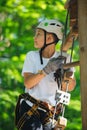Happy, cute, young boy in white t shirt and helmet having fun and playing at adventure park, holding ropes and climbing