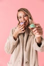 Happy cute young pretty woman posing isolated over pink wall background holding cake macaroons sweeties