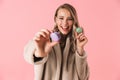 Happy cute young pretty woman posing isolated over pink wall background holding cake macaroons sweeties