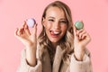 Happy cute young pretty woman posing isolated over pink wall background holding cake macaroons sweeties Royalty Free Stock Photo