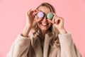 Happy cute young pretty woman posing over pink wall background holding cake macaroons sweeties