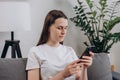 Happy cute young woman sitting on cozy couch using cell phone, smiling lady laughing holding smartphone, looking at cellphone Royalty Free Stock Photo