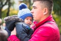 Happy dad holding his son, little funny kid boy on arm, on cold day, standing together in autumn park