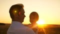 Happy dad holding small daughter in arms of the sun. Dad walks with baby in the meadow at sunset.