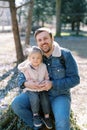 Happy dad with a little girl on his knees sit on a stump in a spring park Royalty Free Stock Photo