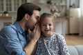 Happy dad sharing secret with excited joyful daughter