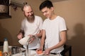 Happy dad and son on kitchen. Smiling father cooking, son washing the dishes. Friendly relationship of parents and teens