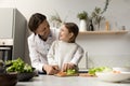 Happy daddy helping cheerful daughter kid to cut fresh vegetables