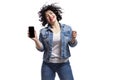 Happy dancing young beautiful girl in jeans shows a smartphone that is emitted on a black screen. Bright brunette with curly hair Royalty Free Stock Photo