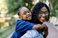 Happy dark skinned African mother holding her child in a park. Smiling cheerful young mother carrying her cute little