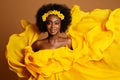 Happy Dark Skinned Woman in Yellow Fashion Dress. Beauty Afro American Model dancing in Silk Gown waving Flying on Wind over Beige