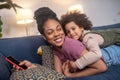 Happy darkskinned mom with daughter lying on sofa