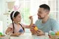 Happy daughter with bunny ears headband and her father having fun while painting Easter eggs Royalty Free Stock Photo