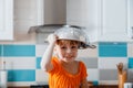 Happy daughter portrait playing in kitchen. Child kid girl Soiled in flour put colander bowl on head like Hat have fun
