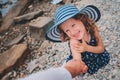 Happy daughter in stripe hat holding mother hand on the beach. Family traveling on summer vacation. Royalty Free Stock Photo