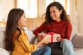 Happy Daughter Surprising Mother Giving Birthday Gift On Couch Indoor