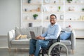 Happy disabled black man in wheelchair using laptop, working online from home, copy space