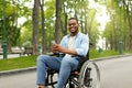 Happy disabled black man in wheelchair using smartphone, checking messages online at park Royalty Free Stock Photo