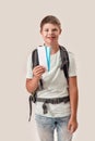 Happy disabled boy with Down syndrome wearing backpack smiling while holding air tickets, standing isolated over white Royalty Free Stock Photo