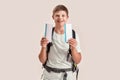 Happy disabled boy with Down syndrome wearing backpack smiling while holding two air tickets, standing isolated over Royalty Free Stock Photo