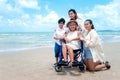 Happy disabled senior elderly woman in wheelchair spending time together with her family on tropical beach. Asian grandma,