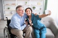 Happy disabled senior man taking selfie with lovely young doctor at home Royalty Free Stock Photo