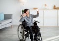 Happy disabled teenager in wheelchair taking selfie on smartphone, smiling at camera indoors Royalty Free Stock Photo