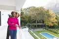 Happy diverse couple embracing, standing on balcony overlooking garden at home, copy space