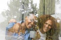 Happy diverse couple sitting on stairs at home, drinking coffee, embracing and looking out of window Royalty Free Stock Photo