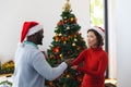 Happy diverse couple wearing santa claus hats, dancing next to christmas tree Royalty Free Stock Photo