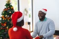 Happy diverse couple wearing santa claus hats, dancing next to christmas tree Royalty Free Stock Photo